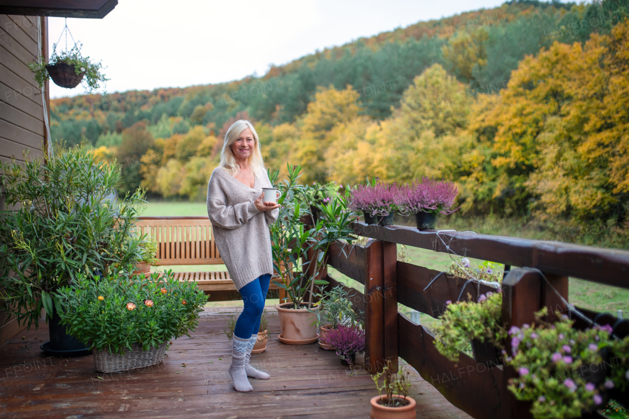 A senior woman with coffee standing outdoors on terrace, looking at camera.