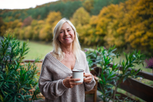 A senior woman with coffee standing outdoors on terrace, looking at camera.