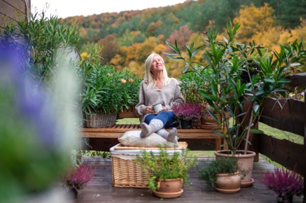 Front view of senior woman with coffee sitting outdoors on terrace, resting.