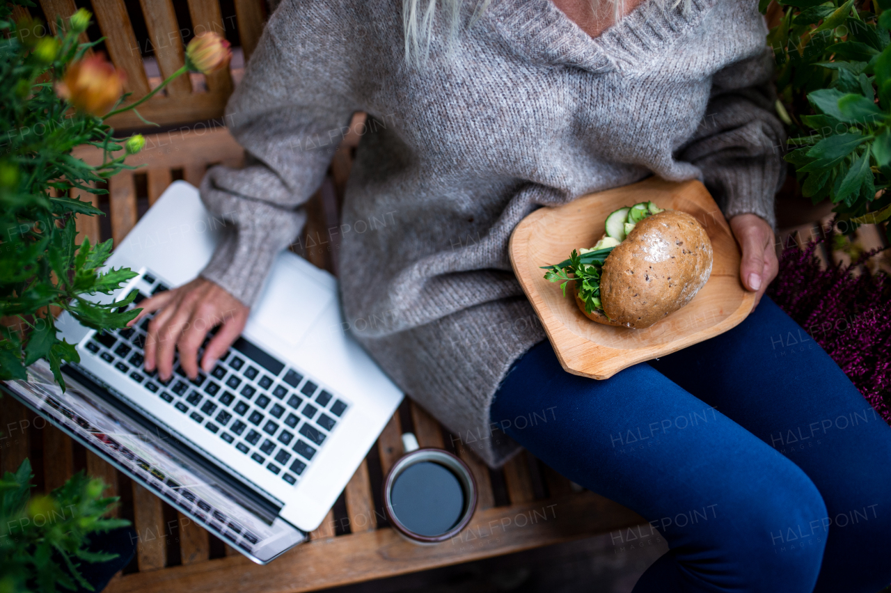 Top view of a senior woman with laptop sitting outdoors on terrace, working.