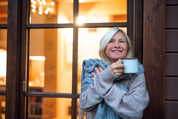 A senior woman with coffee standing outdoors on terrace, resting in the evening.