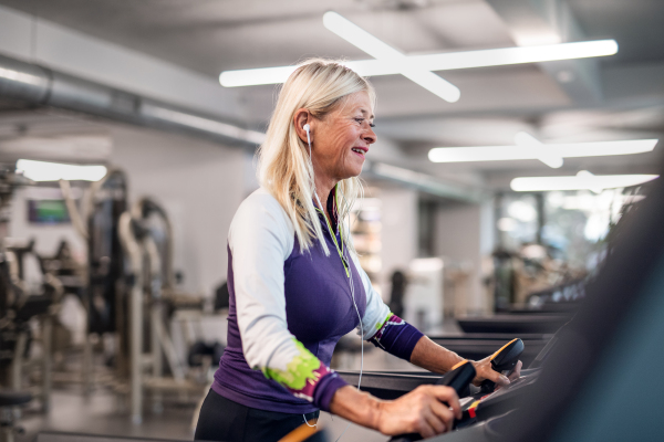 A happy senior woman with earphones in gym doing cardio work out exercise.