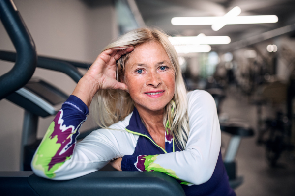 A front view of senior woman in gym resting after doing exercise, looking at camera.