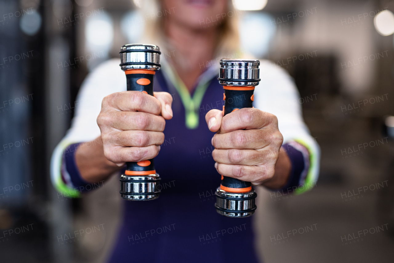 A midsection of unrecognizable senior woman with dumbbells in gym, doing exercise.