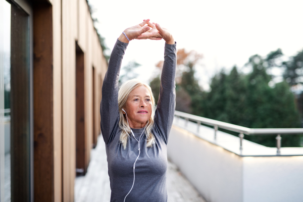 A senior woman with earphones outdoors doing exercise on terrace.