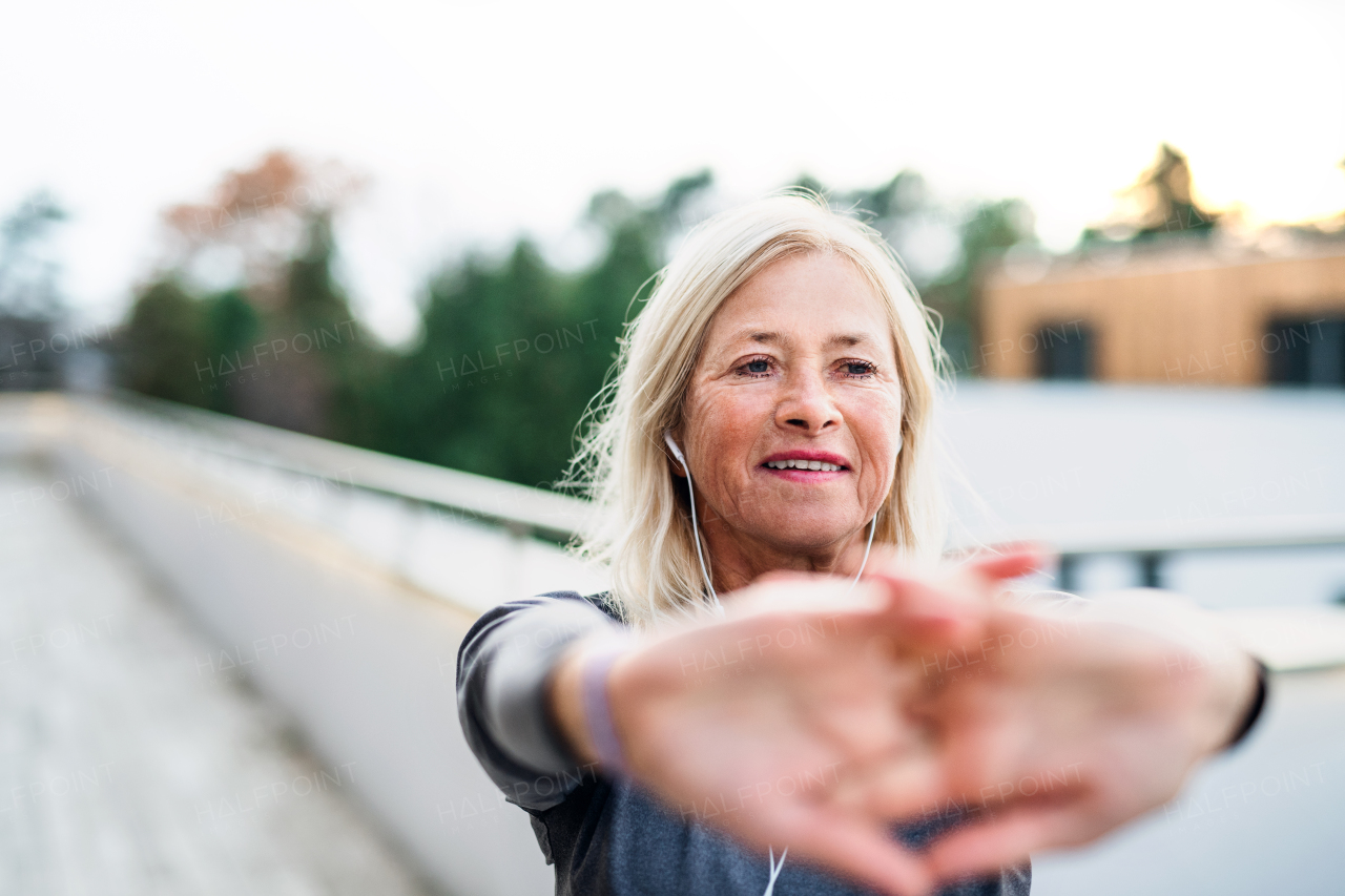 A senior woman with earphones outdoors doing exercise on terrace.