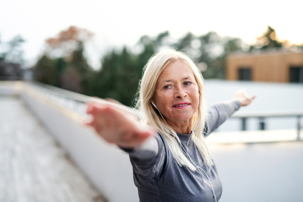 A senior woman with earphones outdoors doing exercise on terrace.