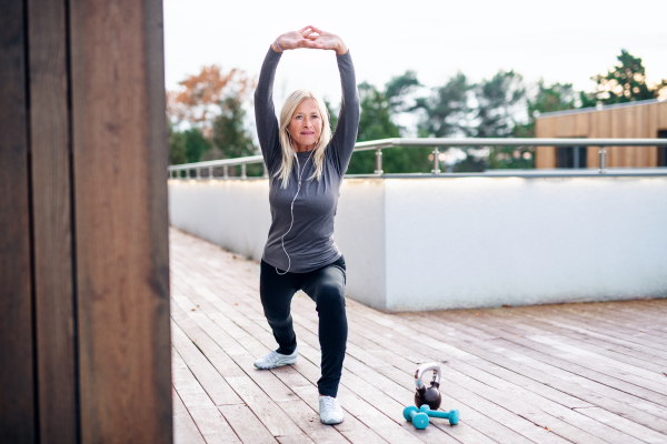 A front view of senior woman doing exercise outdoors, stretching.