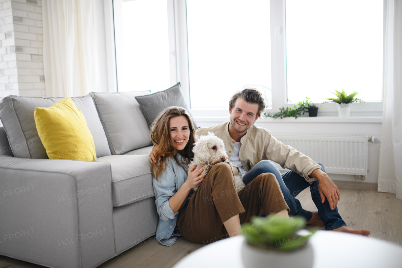 A happy young couple in love with dog sitting indoors at home, looking at camera.