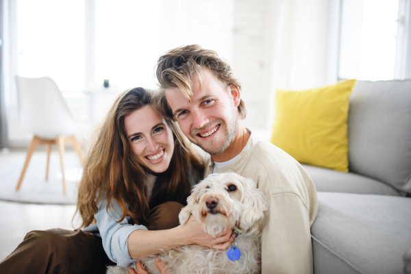 A happy young couple in love with dog indoors at home, looking at camera.