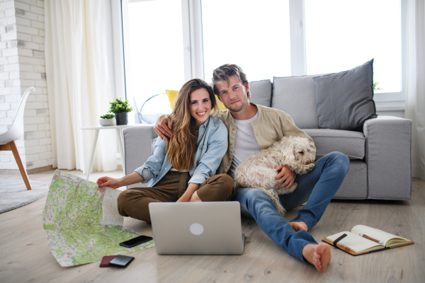 A happy young couple in love with dog planning holidays indoors at home, looking at camera.