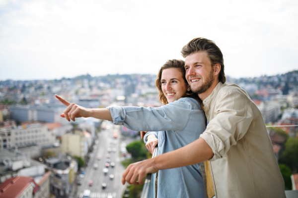 A happy young couple in love standing outdoors on balcony at home, hugging and talking.