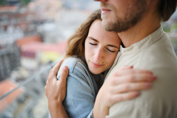 A happy young couple in love standing outdoors on balcony at home, hugging.