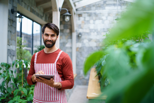 Low angle view of man gardener with tablet standing in greenhouse, working.