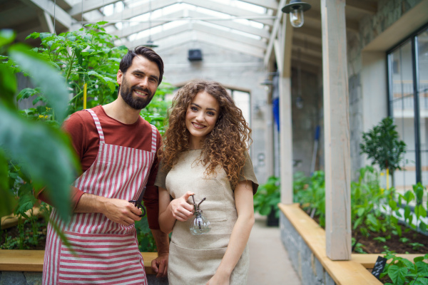 Portrait of man gardener with apron standing in greenhouse, looking at camera.