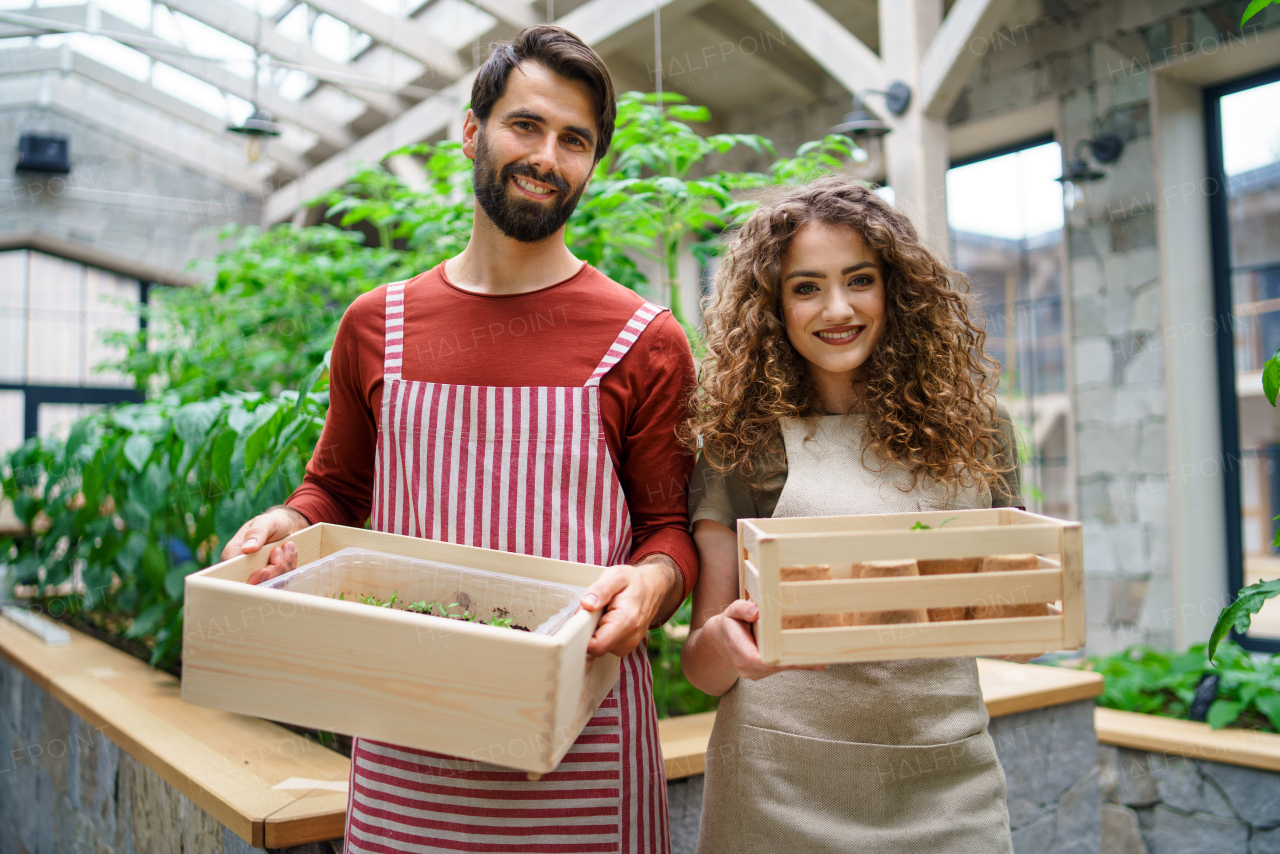 Front view portrait of man and woman gardeners standing in greenhouse, looking at camera.