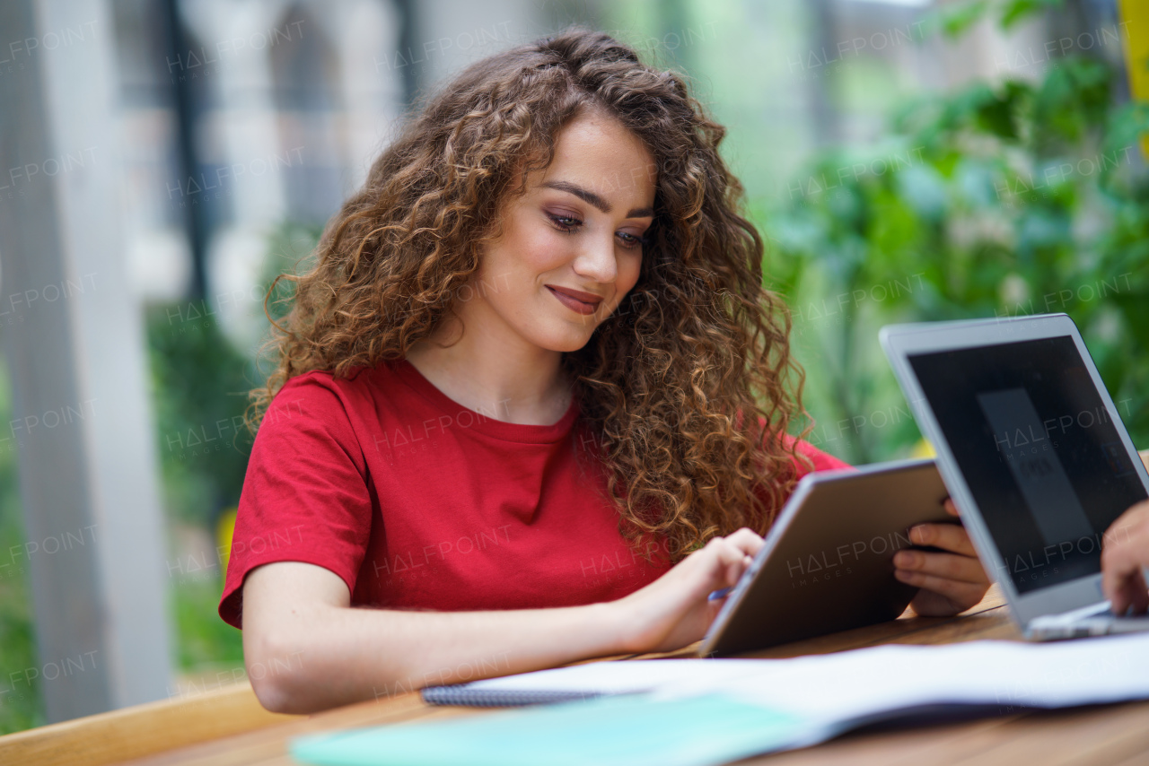 Portrait of young woman with tablet sitting indoors in office, working.