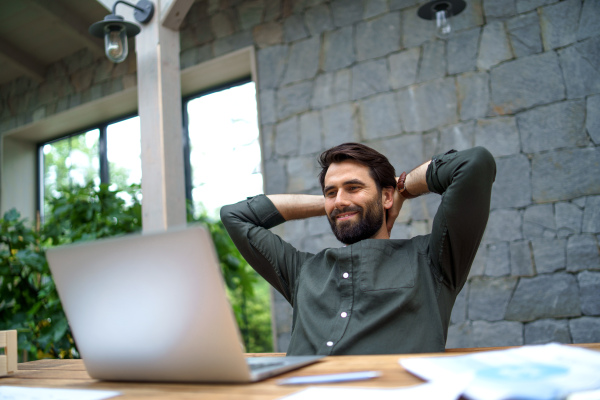 Portrait of young man with laptop sitting indoors in office, working.