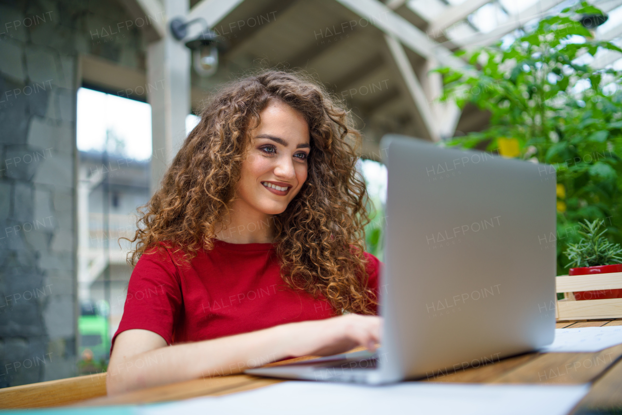 Portrait of young woman sitting indoors in office, using laptop.