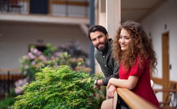 Happy young couple standing outdoors on hotel balcony on holiday, relaxing.