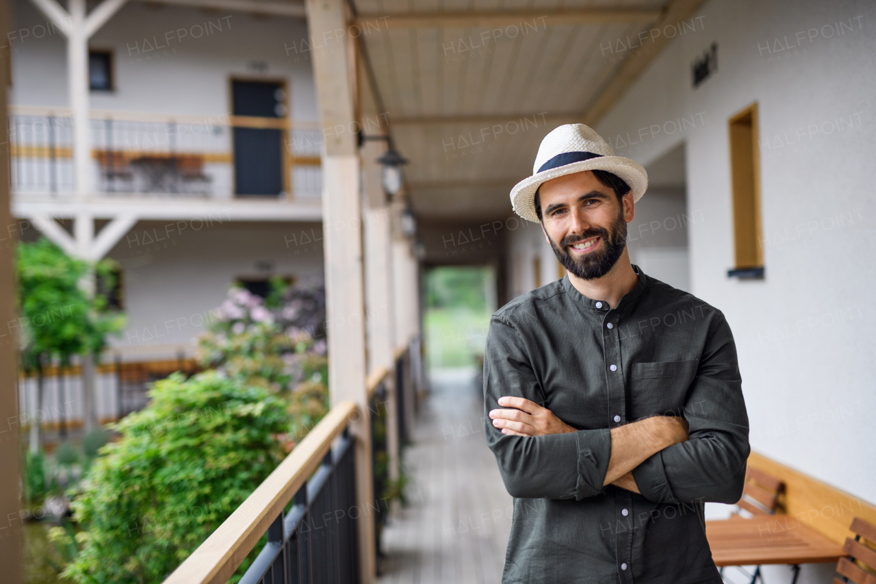 Front view of young man standing outdoors by hotel on holiday, looking at camera.