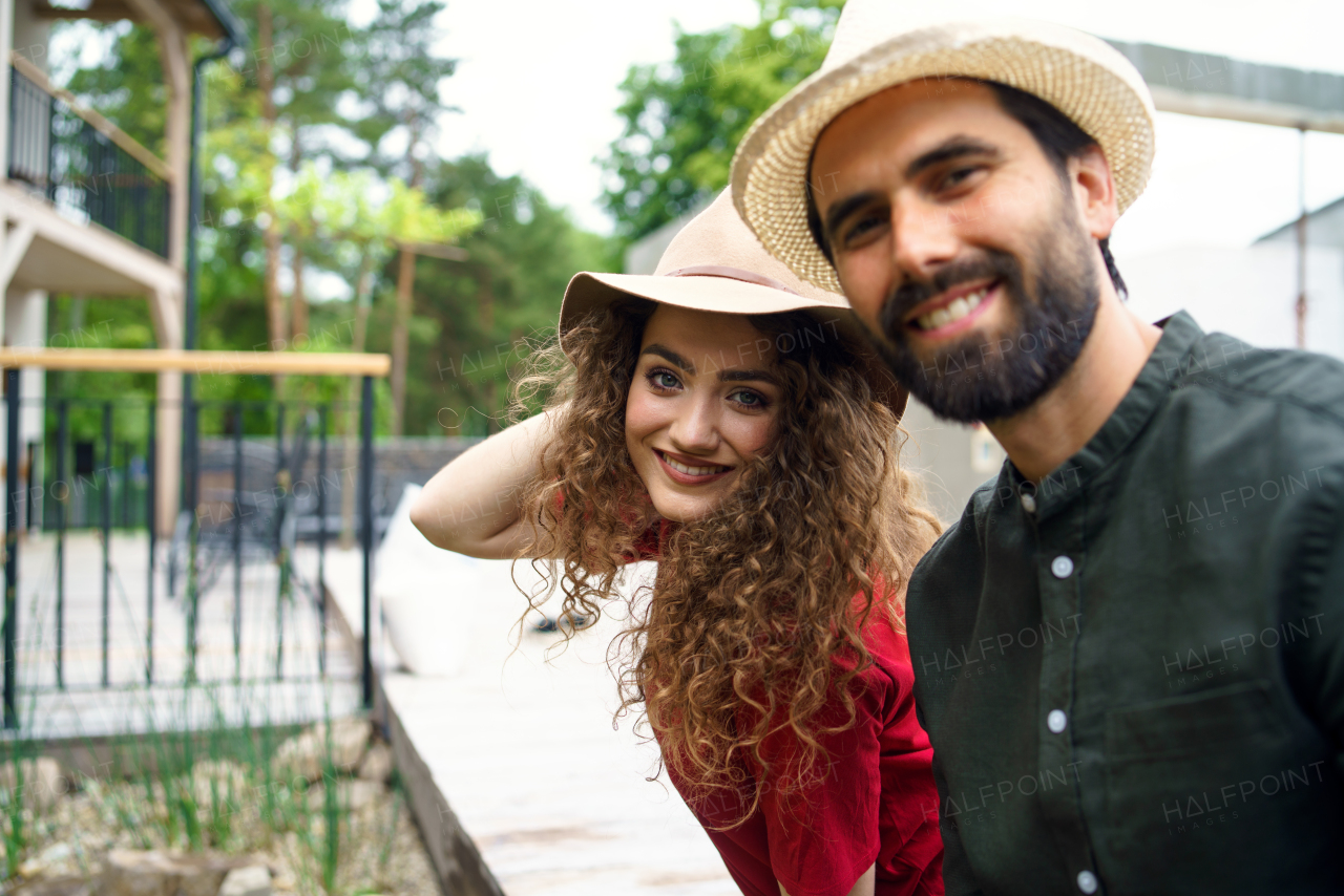 Portrait of young couple standing outdoors by hotel on holiday, looking at camera.