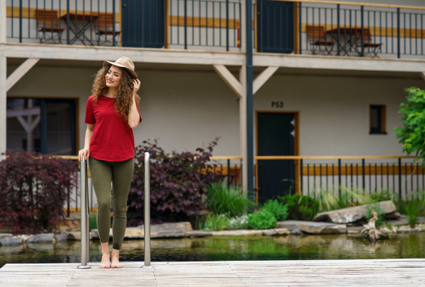 Happy young woman standing outdoors by hotel on holiday, relaxing.