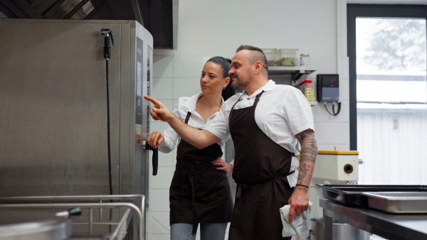 A chef teaching cook how to use combi oven indoors in restaurant kitchen.