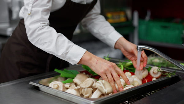 A close-up of cook washing vegetables in sink in commercial kitchen.