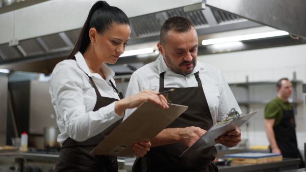 A chef and cook discussing menu indoors in restaurant kitchen.