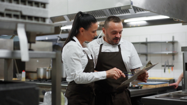 A chef and cook discussing menu indoors in restaurant kitchen.