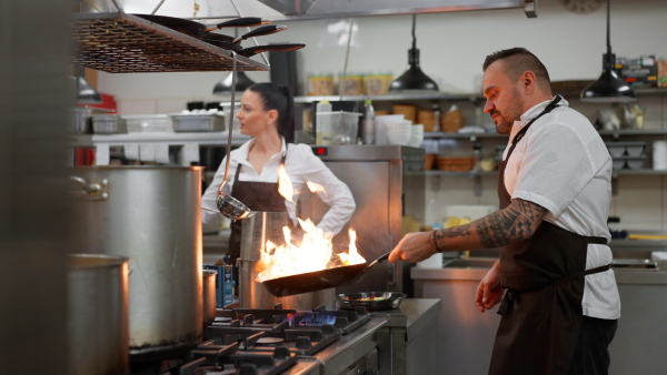 A professional chef preparing meal, flambing indoors in restaurant kitchen.