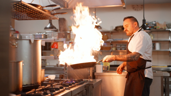 A professional chef preparing meal, flambing indoors in restaurant kitchen.