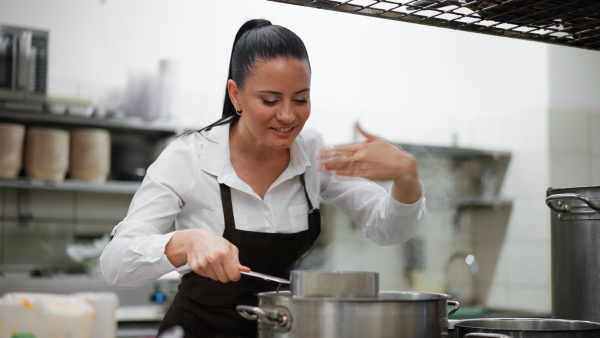 A happy female chef cooking indoors in restaurant kitchen.