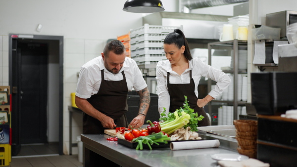 A chef teaching how to cook, cutting vegetables indoors in commercial kitchen.