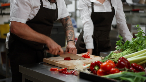 A close-up of unrecognizable chef cutting vegetables indoors in commercial kitchen.