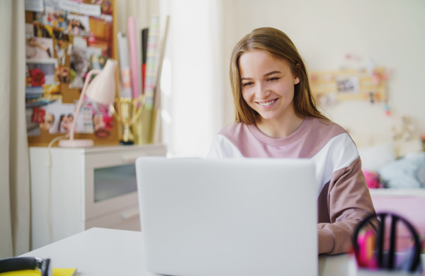 Front view of young female student sitting at the table, using laptop in quarantine.