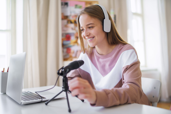 Young female student with laptop and microphone sitting at the table, online lesson concept.