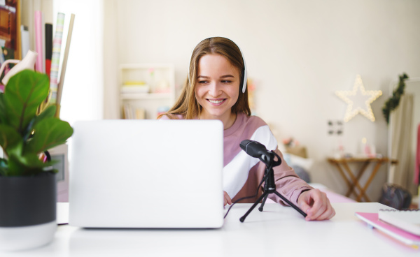 Young female student with laptop and microphone sitting at the table, online lesson concept.