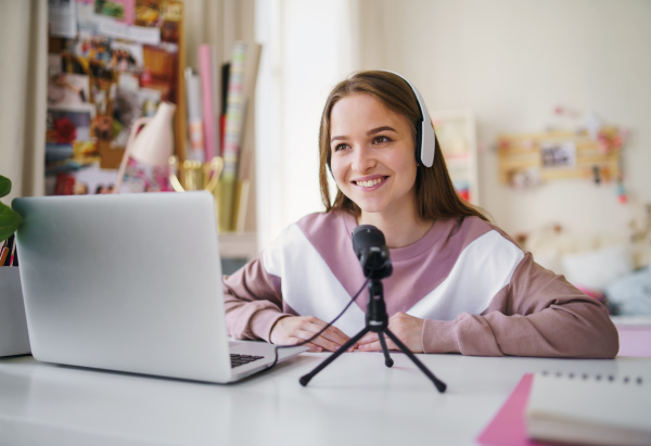 Young female student with laptop and microphone sitting at the table, online lesson concept.