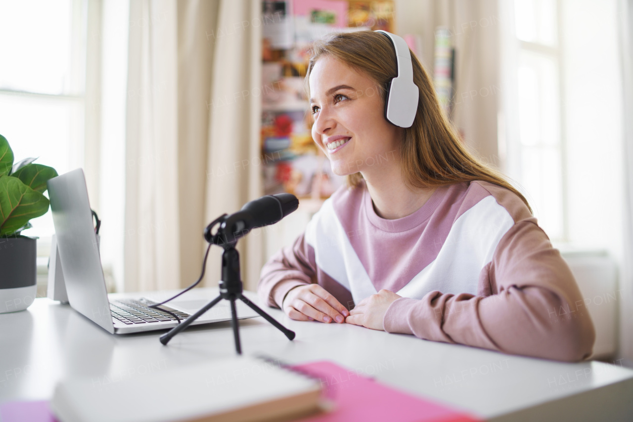 Young female student with laptop and microphone sitting at the table, online lesson concept.