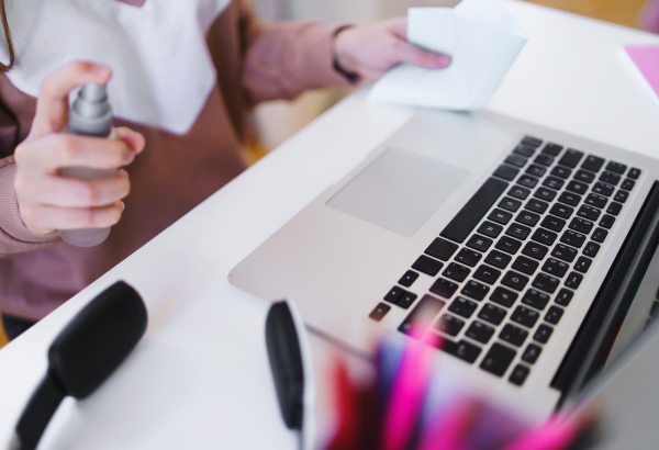 Midsection of unrecognizable young student with gloves at the table, disinfecting laptop.