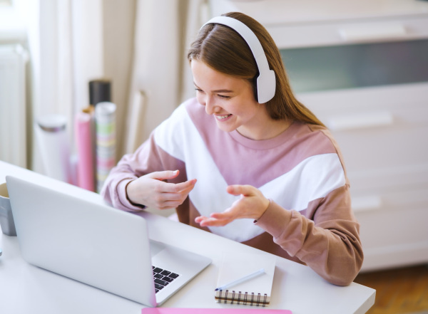 Young female student with headphones and laptop at the table, online lesson concept.