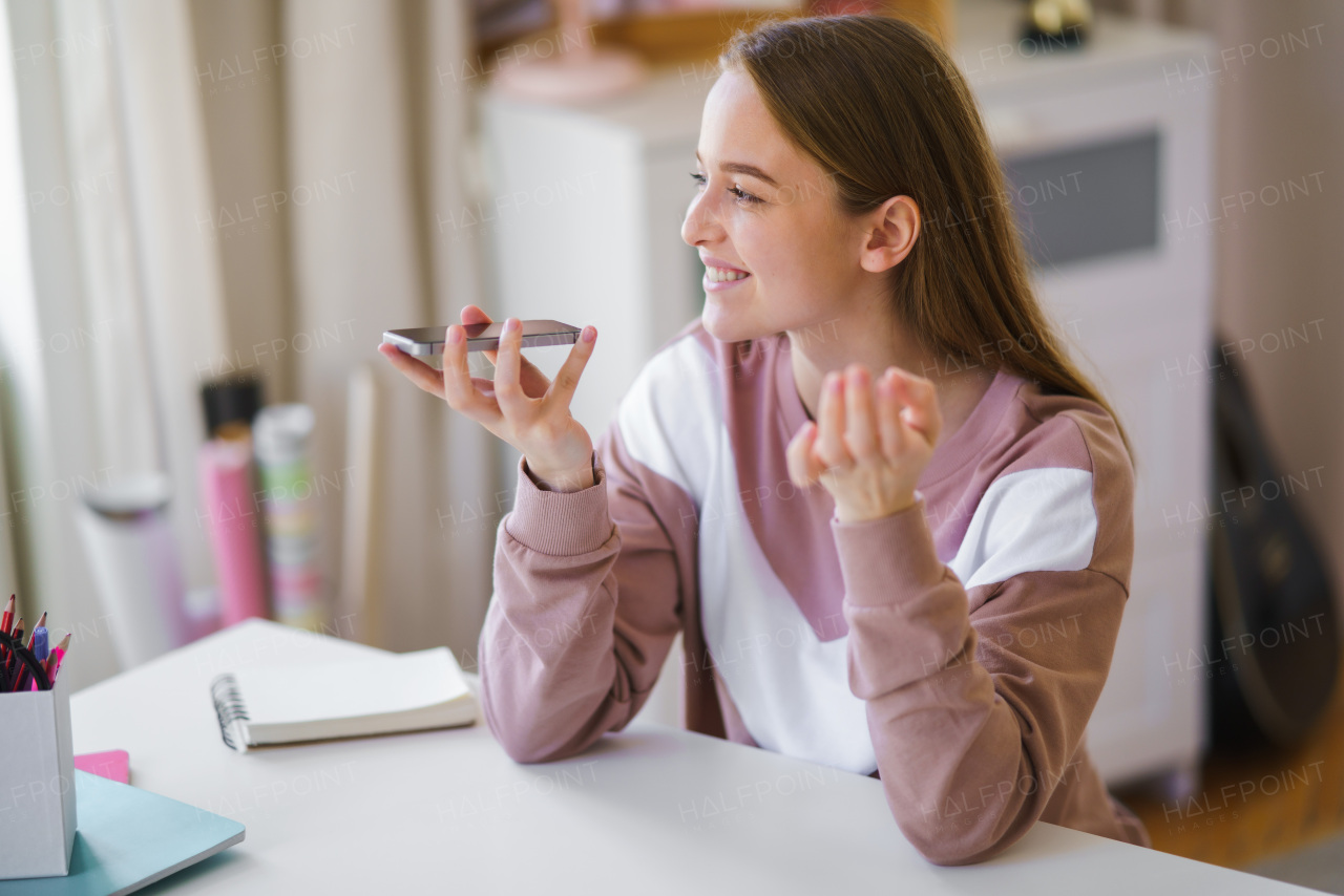 Young female student with smartphone sitting at the table, online lesson concept.