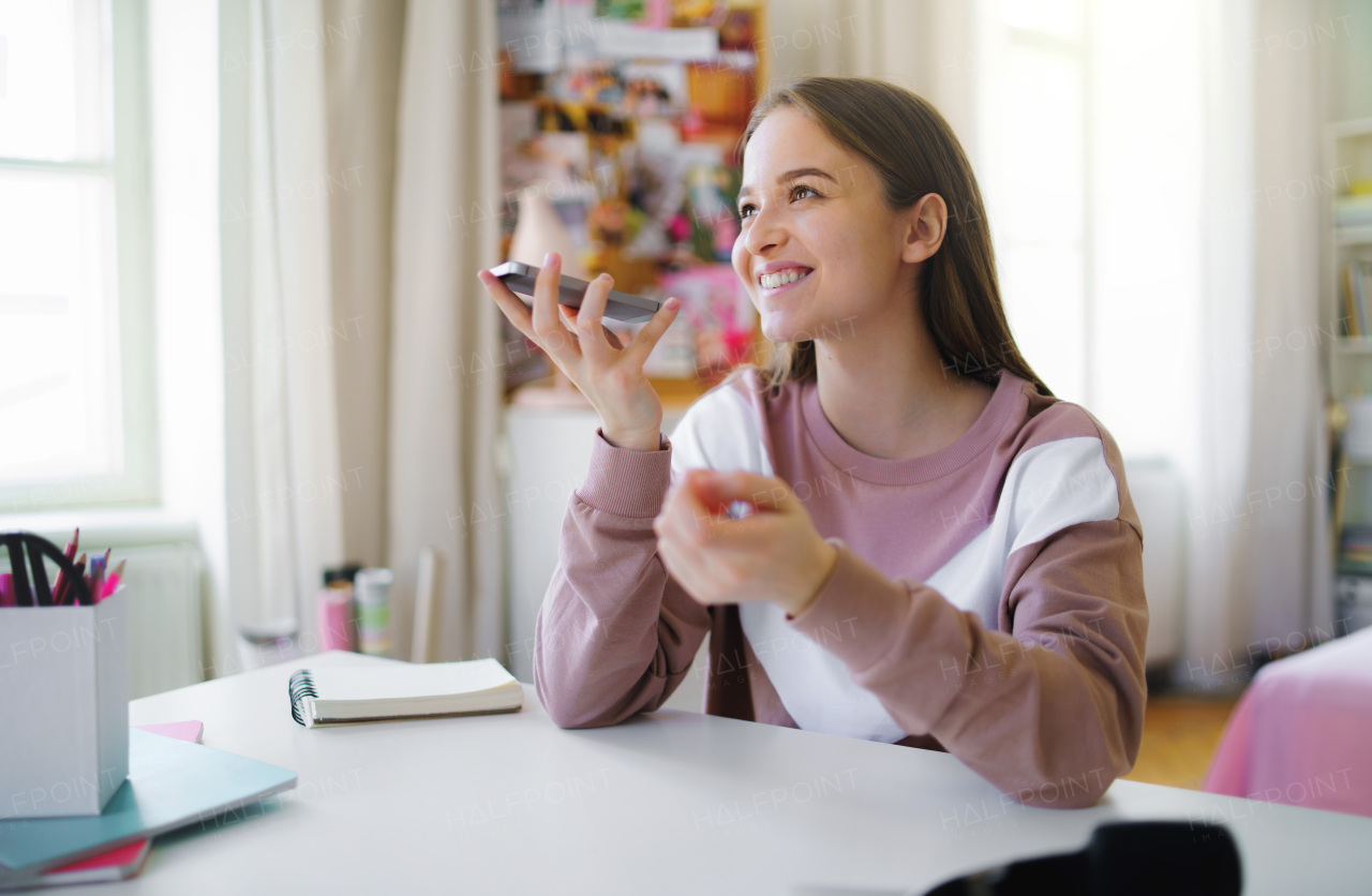 Young female student with smartphone sitting at the table, online lesson concept.