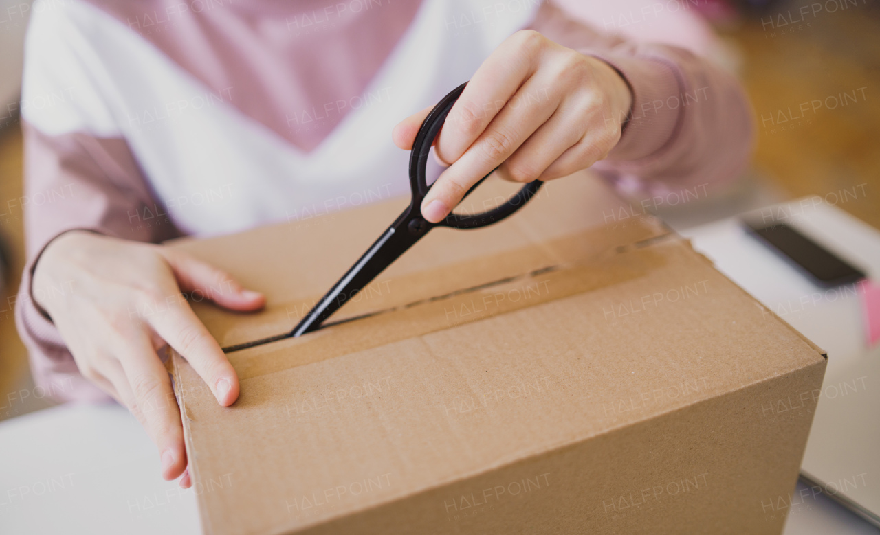 Midsection of unrecognizable young womant at the table, opening parcel box.