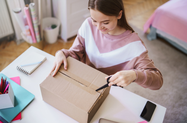 Front view of young female student at the table, opening parcel box.