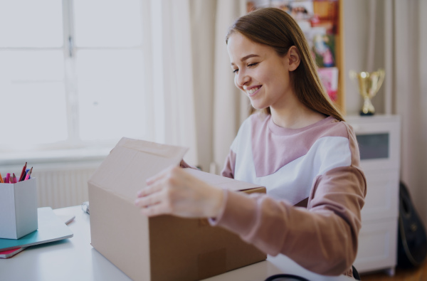 Side view of young female student at the table, opening parcel box.