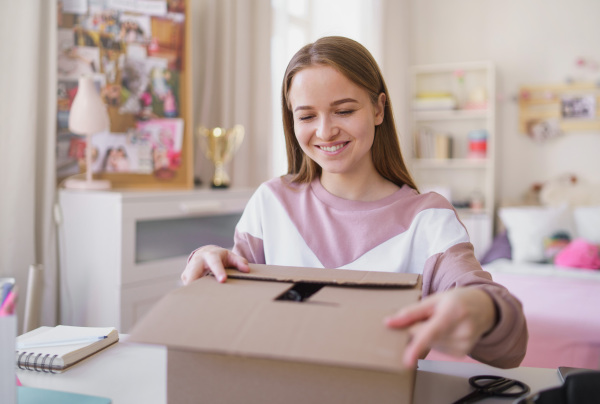 Front view of young female student at the table, opening parcel box.