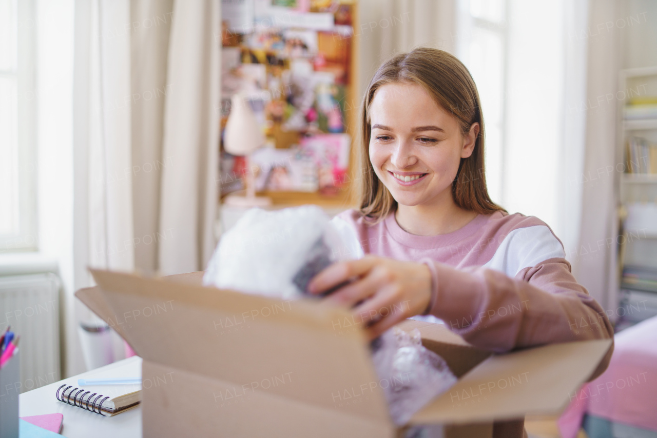 Front view of young female student at the table, opening parcel box.